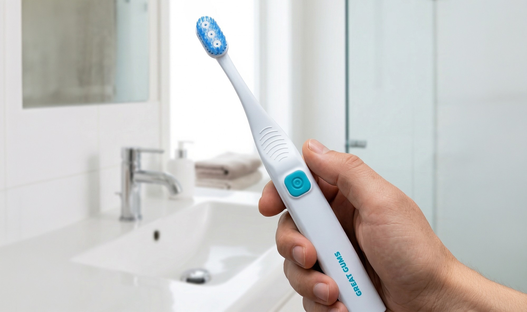 Hand holding Great Gums toothbrush in front of a bathroom sink